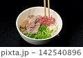 Adding fresh raw beef slices into pho bowl with wooden chopsticks, traditional Vietnamese beef noodle soup preparation 142540896