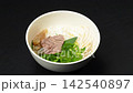 Adding tender cooked beef brisket slices and tendon into pho noodle bowl with wooden chopsticks, Vietnamese noodle soup cooking 142540897