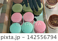 Pastry Shop Worker Arranging Colorful Macarons on Glass Display Tray Preparing Elegant Dessert Showcase for Customers 142556794