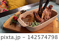 Roasted Half Duck Served with Microgreens on a Wooden Board with Fork and Knife in Elegant Restaurant Presentation 142574798