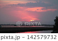 Scenic view of the Venetian Lagoon during a dramatic sunset, featuring a vibrant pink and purple sky reflecting on the calm water and marshlands, with a distant industrial silhouette on the horizon in Scenic view of the Venetian Lagoon during a dramatic sunset, featuring a vibrant pink and purple sky reflecting on the calm water and marshlands, with a distant industrial silhouette on the horizon in 142579732