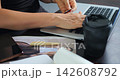 Closeup hands holding card near laptop, coffee cup and notebook on desk entering card details for online purchase in cozy cafe setting with soft natural light and casual workspace objects. 142608792