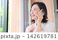 A video showing a woman, possibly a housewife in her 50s, smiling and talking on her smartphone at home, chatting with family and friends in between household chores. 142619781