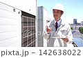 A man in work clothes walks towards the camera, inspecting the air conditioning equipment. 142638022