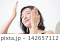 A beauty portrait of a woman in her 50s with beautiful skin, featuring skincare and anti-aging imagery as she touches her cheek. 142657112