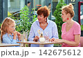 Mother, daughter and grandmother are having a warm conversation, sitting at a cafe table 142675612