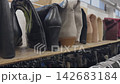 A variety of used footwear, including boots and heels, are arranged on a wooden shelf in a clothing store. The shoes show different colors and styles, highlighting the selection available 142683184