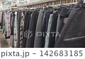 A collection of skirts and pants hangs on racks in a used clothing store, showcasing a variety of patterns and colors, with visible tags and hangers in a well-organized retail space 142683185