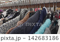 Close-up view of a clothing rack in a used clothing store, displaying a variety of sweaters and garments in different colors and textures, highlighting the selection available for shoppers 142683186