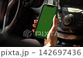 Female hand Holding Mobile Phone with Green Chroma Key Screen Mockup inside Modern Car. Cellphone display close up. Business mockup empty blank space. VFX Motion Tracking Markers. 142697436
