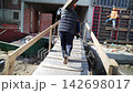 Worker carries beam on shoulder as walks along bridge 142698017