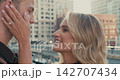Close-up of a happy loving couple looking into each others eyes and smiling against the backdrop of big city buildings at sunset. Genuine emotions, romance. Slow motion. 142707434