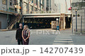 A romantic moment of a loving couple. The man approaches his beloved from behind and gently hugs her by the shoulders against an urban architecture background. 142707439