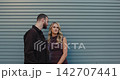 An emotional shot of a loving couple standing against a modern gray wall. The man gently kisses his woman, and she smiles sincerely. 142707441