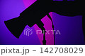 Silhouette of a man setting up a studio spotlight on a stand against a bright, color changing background with fractures. Camera operator backstage. 142708029