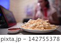 A woman enjoying karaoke with a plate of french fries on the table. 142755378