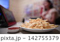 A woman enjoying karaoke with a plate of french fries on the table. 142755379
