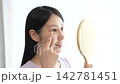 A woman with eyelash extensions looks in the mirror. 142781451