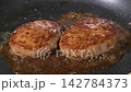 黒いフライパンでソースがかかった2個のハンバーグが煮詰まる様子の動画 142784373