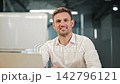 Confident Businessman Smiles at Camera From Office Desk 142796121