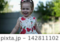 Beautiful happy child dancing and playing on green grass lawn outdoor. Pretty small girl spinning in her summer dress at sunny garden. Carefree kid enjoying playful childhood moments at nature 142811102