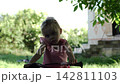 Cute small girl in pink dress riding bicycle through green summer garden. Beautiful blonde child steering balance bike outdoor on sunny day. Pretty kid enjoying active recreation and childhood moments 142811103
