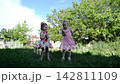 Two pretty small girls dancing together on the green grass lawn. Happy little children spinning in beautiful dresses in a sunny garden. Carefree sisters enjoying playful childhood moments at nature 142811109