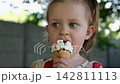 Portrait of attractive small girl eating delicious ice cream in a waffle cone outdoor. Beautiful child biting cold sweet dessert in summer garden. Cute kid enjoying tasty refreshing food on sunny day 142811113