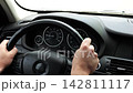Male arms holds steering wheel while driving a motor car at city. Young man riding on electric automobile at urban road. Driver moving on his electrical auto on route. Slow motion 142811117