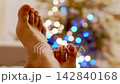 Person feet laying against lit Christmas tree with garlands 142840168