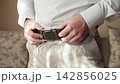 Man preparing for his wedding day by adjusting his belt in a bright room 142856025