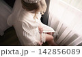 Bride getting ready on her wedding day in a room with bright curtains and a soft light coming through the window 142856089
