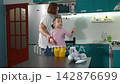 A young Caucasian mother cares for her little daughter at home, gently wiping her face while the girl stands on a small stool. The scene represents attentive parenting and daily childcare 142876699