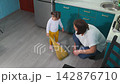 Caucasian female educator helps a little girl learn sweeping during a kindergarten cleaning activity. The lesson supports early childhood development, motor skills, and Montessori education. Top view. 142876710