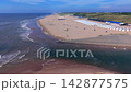 Wide horizontal aerial drone video of Katwijk water outlet channel, North Sea foam waves, sandy beach, white resort cabins, and green sand dunes in South Holland, Netherlands on late afternoon 142877575