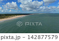 Wide horizontal aerial drone video of sandy beach coastline, North Sea turquoise water, coastal sand dunes, white cumulus clouds, and blue sky in Burgh-Haamstede, Zeeland, Netherlands on sunny day 142877579