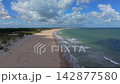 Wide horizontal aerial drone video of sandy beach coastline, North Sea foam waves, cloud shadow across golden sand, dunes, and cumulus cloud sky in Burgh-Haamstede, Zeeland, Netherlands on sunny day 142877580