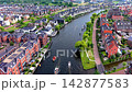Wide horizontal aerial drone video of residential canal district, modern waterfront houses, small motorboats cruising, solar roof panels, and green park paths in Leiden, South Holland, Netherlands 142877583