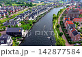 Wide horizontal aerial drone video of residential canal district, small motorboat cruising, modern waterfront houses, solar roof panels, and green park paths in Leiden, South Holland, Netherlands 142877584