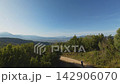Woman hiking peaceful mountain trail through alpine forest with expansive valley vista 142906070