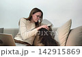 Owner gently pets maine coon cat while sitting together on sofa at home. Large fluffy feline enjoys interaction and stays calm indoors. Pet affection comfort and bonding lifestyle concept.. 142915869