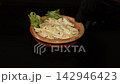 Close-up shot of a chef in black gloves presenting and adjusting a clay bowl of creamy German potato salad with cucumber slices on a dark background. 142946423