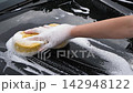Close-up of a hand washing a black car with a soapy sponge, creating rich foam during vehicle cleaning, showcasing automotive care, maintenance, and detailing 142948122