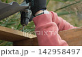 Construction drilling roofing worker secures metal sheet onto wooden frame using a cordless power tool. 142958497