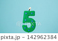 Number five birthday candle burning and gradually extinguishing against a light blue background, symbolizing a fifth birthday celebration and anniversary milestone. 142962384