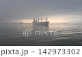 一艘大型貨輪航行在晨霧籠罩的海面上，沐浴在晨光中。從船上看到的海洋物流和貿易景象。背景影片素材。 142973302