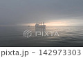 一艘商船停泊在波濤洶湧的大海上，沐浴在透過雲層的柔和陽光中——這是從船上拍攝到的如夢似幻、寧靜祥和的清晨海景。 142973303
