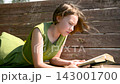 Teenage schoolgirl studying reading her books, lying down outdoors. 143001700