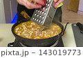 Close-up view of hand stirring chicken and vegetable stew simmering in cast iron skillet on kitchen stove, steam drifting upward and warm light highlighting thick yellow broth texture 143019773