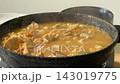 Creamy chicken stew lifted by spoon in cast iron pot as steam rises, showing tender chicken pieces and carrot chunks in warm kitchen light 143019775